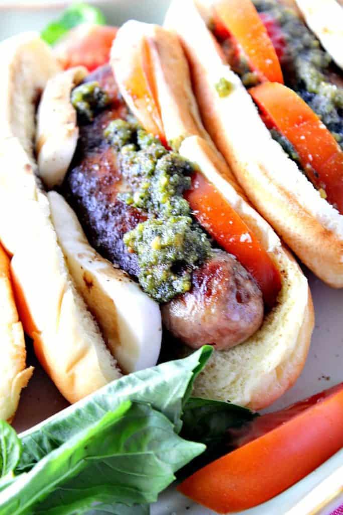 Vertical closeup image of an Italian sausage Caprese sandwich with basil pesto, fresh tomatoes, and mozzarella cheese.