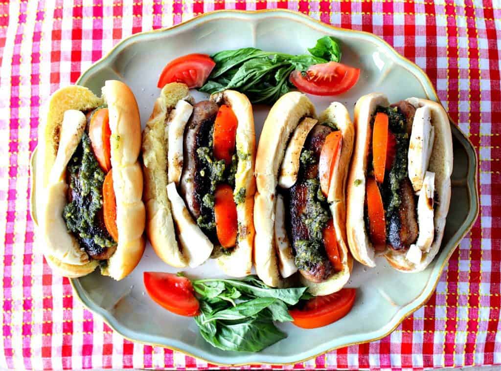 Overhead photo of 4 Caprese Sausage Sandwiches on a platter with a red and white checkered napkin.