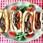 Overhead photo of 4 Caprese Sausage Sandwiches on a platter with a red and white checkered napkin.