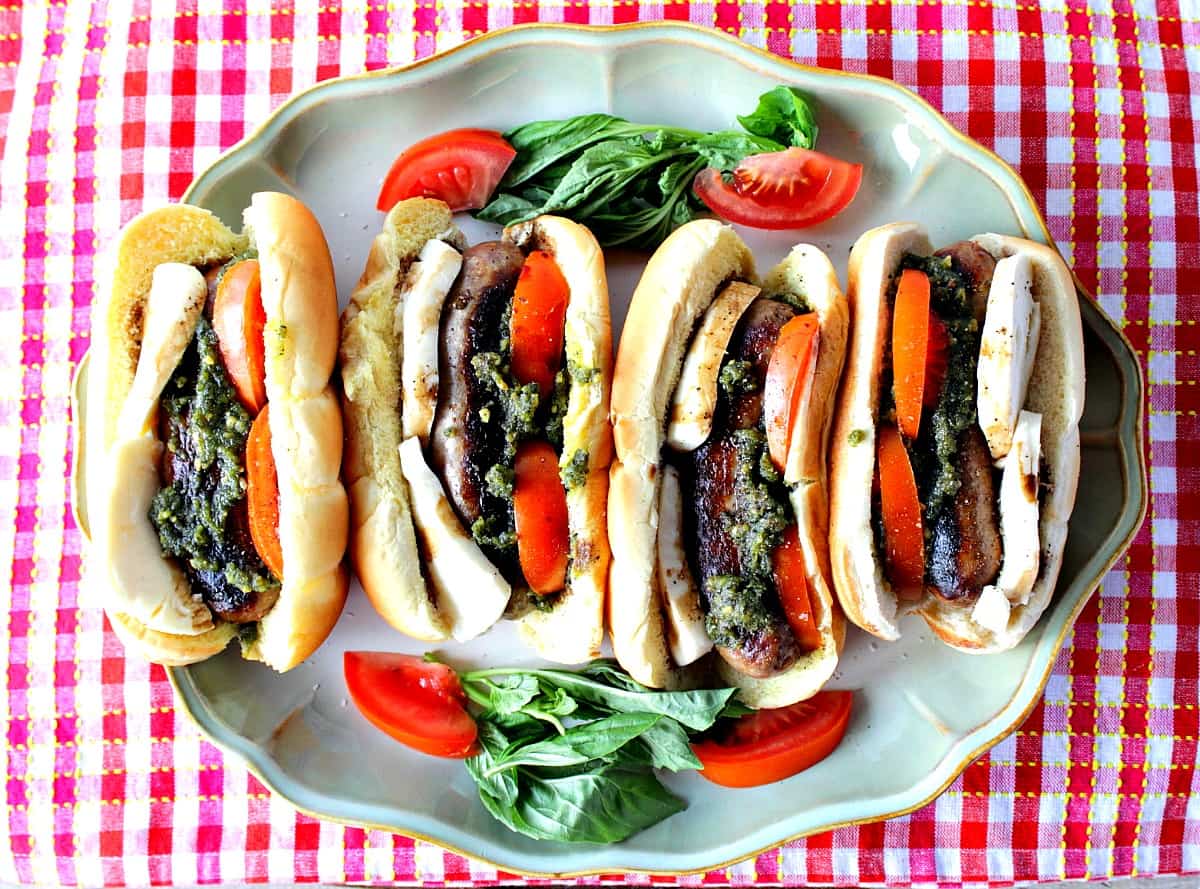 Overhead photo of 4 Caprese Sausage Sandwiches on a platter with a red and white checkered napkin.