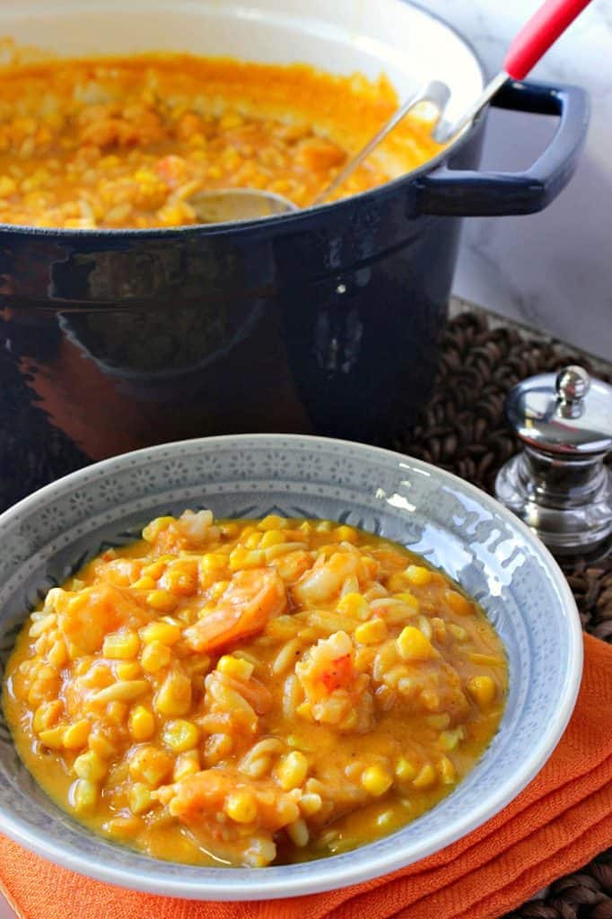 A vertical photo of a blue bowl filled with pumpkin corn chowder and a pepper shaker and blue pot in the background.