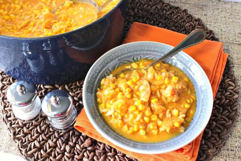 An overhead photo of a bowl of pumpkin corn chowder with a spoon and a blue pot with a ladle.