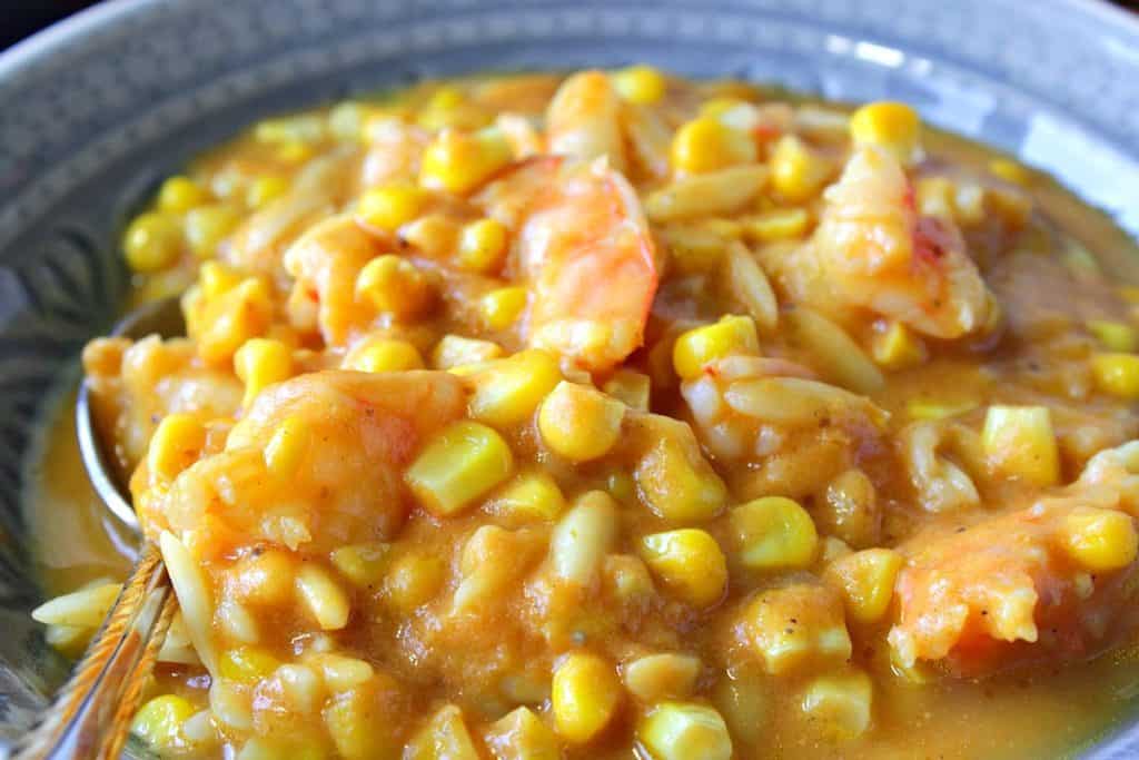 A closeup photo of corn chowder with pumpkin, orzo pasta and shrimp in a bowl.