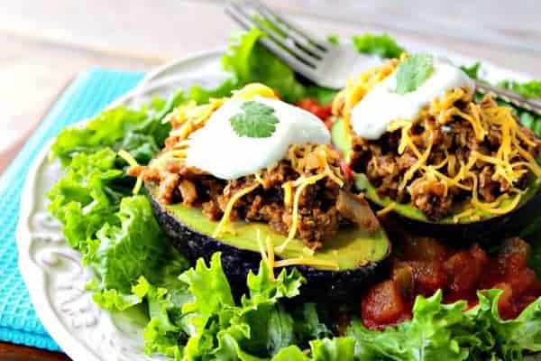 Two turkey taco stuffed avocado halves on a white plate with lettuce and salsa.