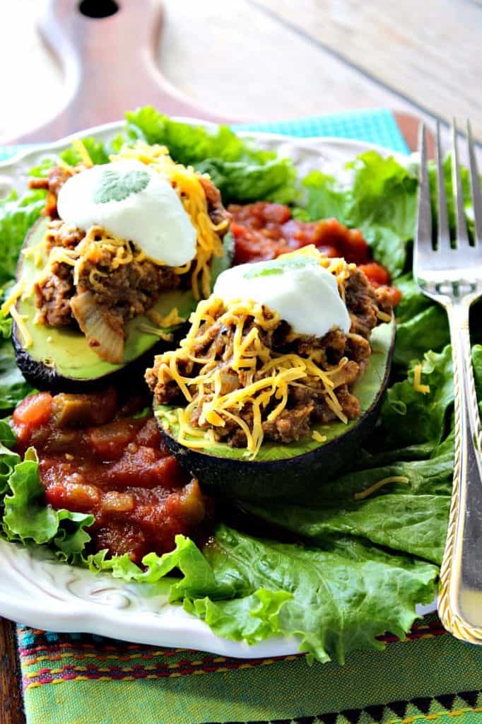 Vertical image of two stuffed avocados on a bed of lettuce with cheese and sour cream on top.