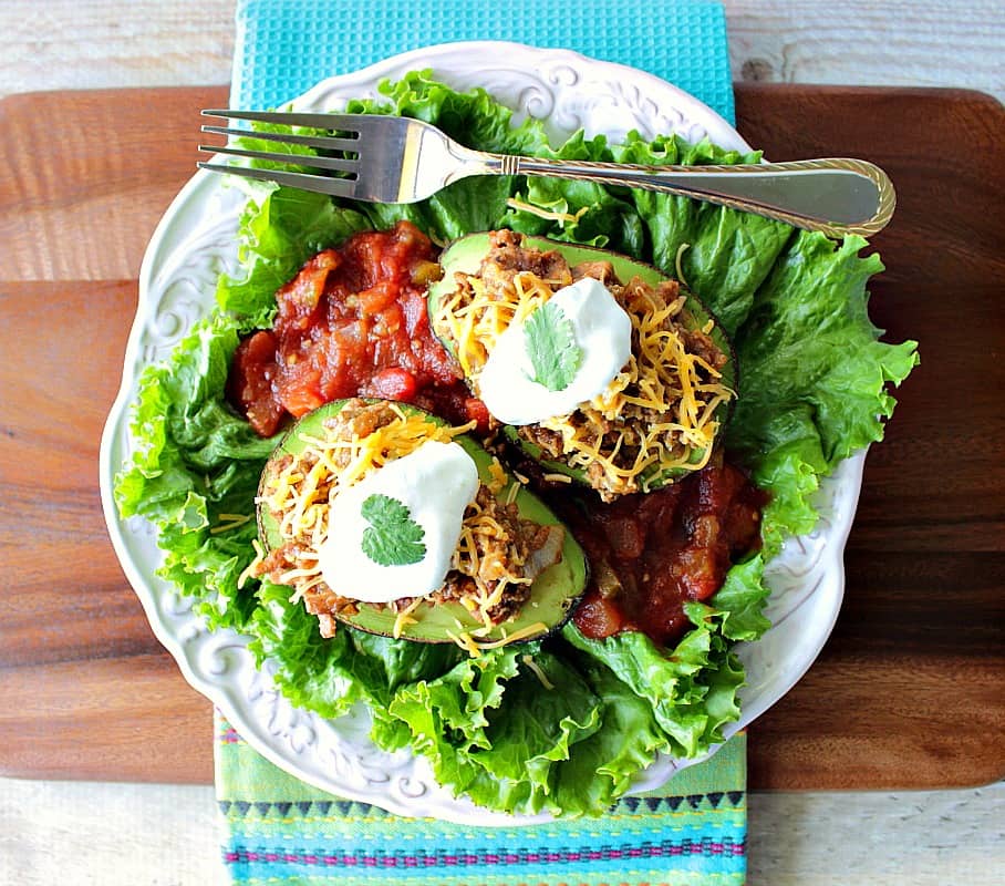 Overhead photo of two turkey taco stuffed avocados on a white plate with lettuce and salsa.