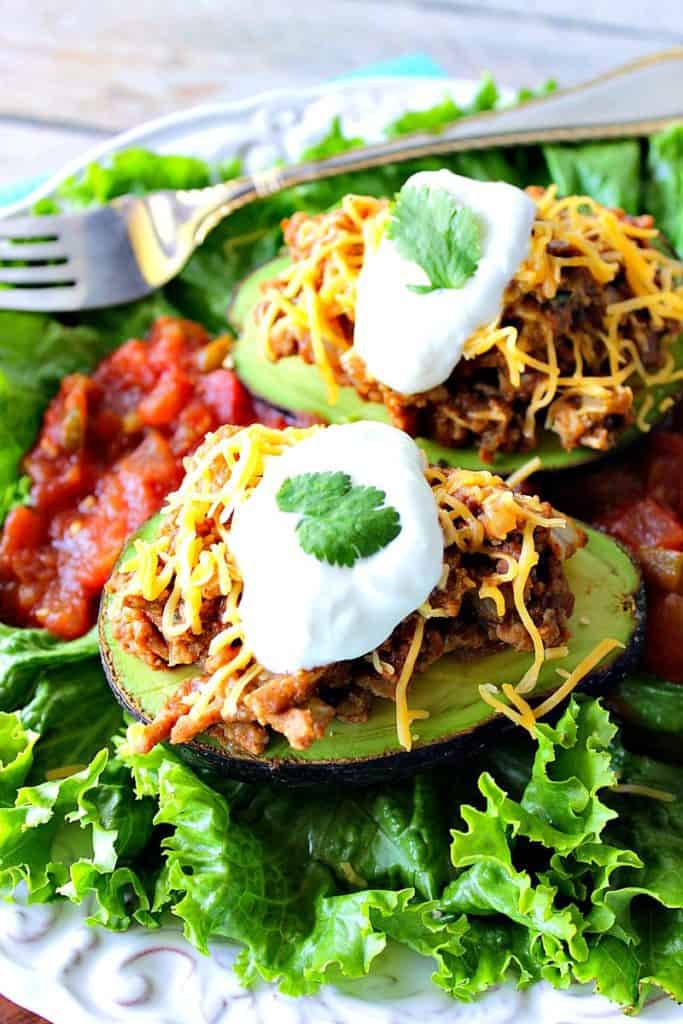 Vertical closeup image of two stuffed avocados with ground turkey, shredded cheese, and sour cream.