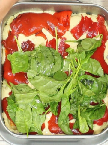An overhead photo of the making of Alfredo Ravioli Lasagna with red peppers, spinach, and basil.