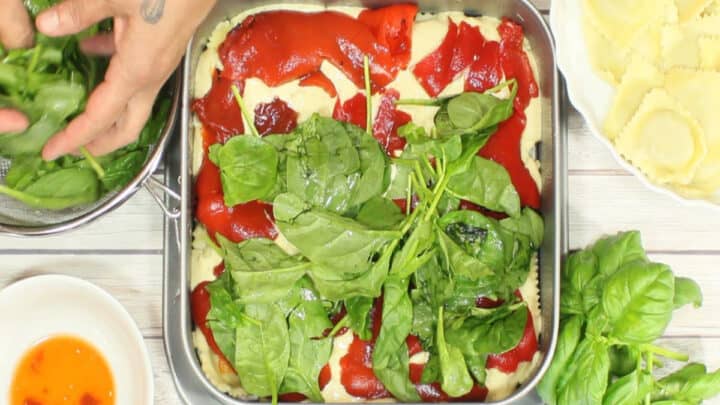 An overhead photo of the making of Alfredo Ravioli Lasagna with red peppers, spinach, and basil.