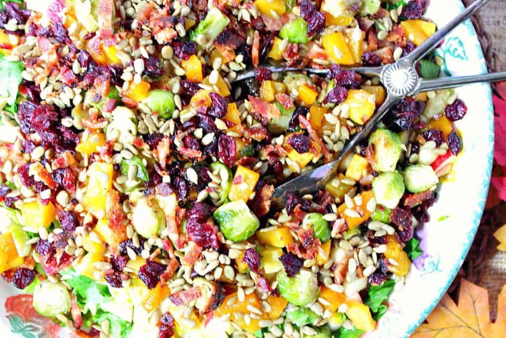Overhead colorful photo of a fall chopped salad with tongs and jewel tone veggies and fruit.