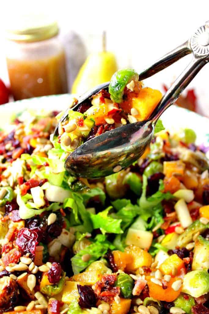 Closeup vertical photo of salad tongs holding a serving of Thanksgiving chopped salad.