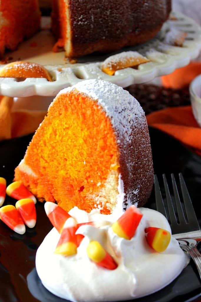 A closeup vertical photo of a slice of candy corn colored pound cake on a plate with whipped cream and candy corn.