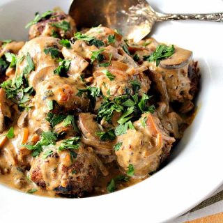 A large white bowl filled with German meatballs with caraway mushroom cream sauce, parsley, and a large serving spoon.