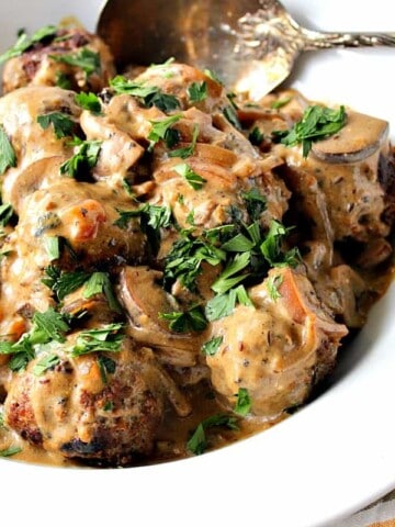 A large white bowl filled with German meatballs with caraway mushroom cream sauce, parsley, and a large serving spoon.