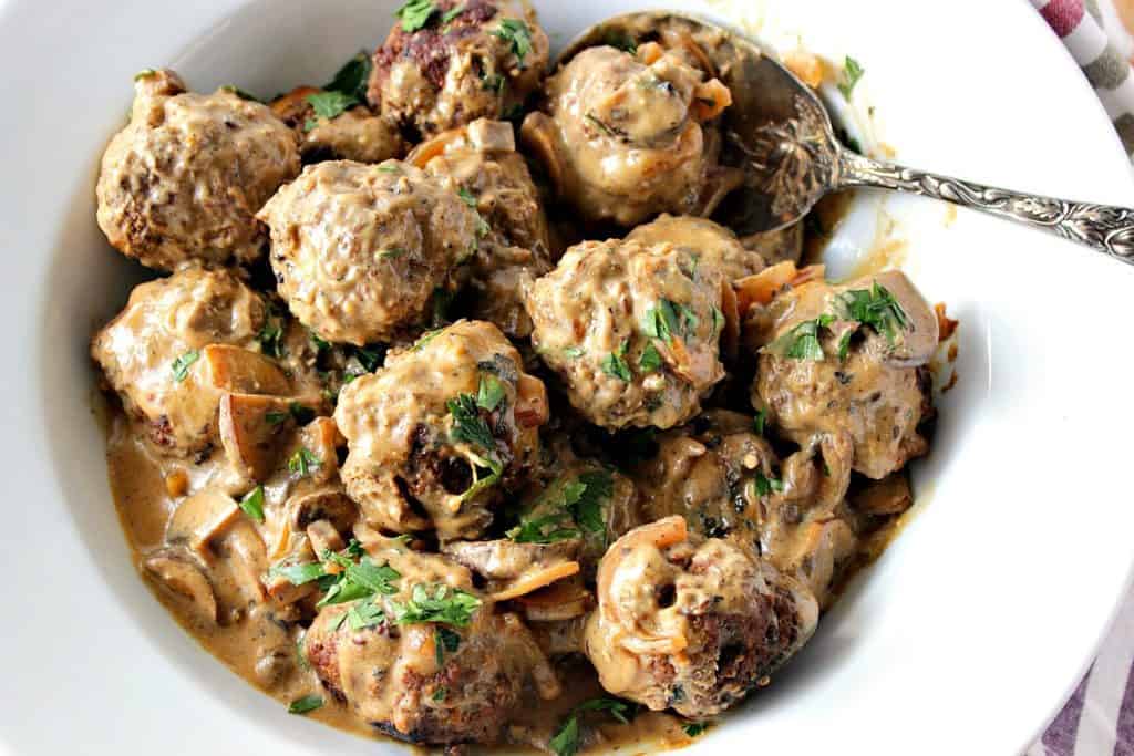 Overhead photo of a bowlful of German meatballs with parsley and a large serving spoon.