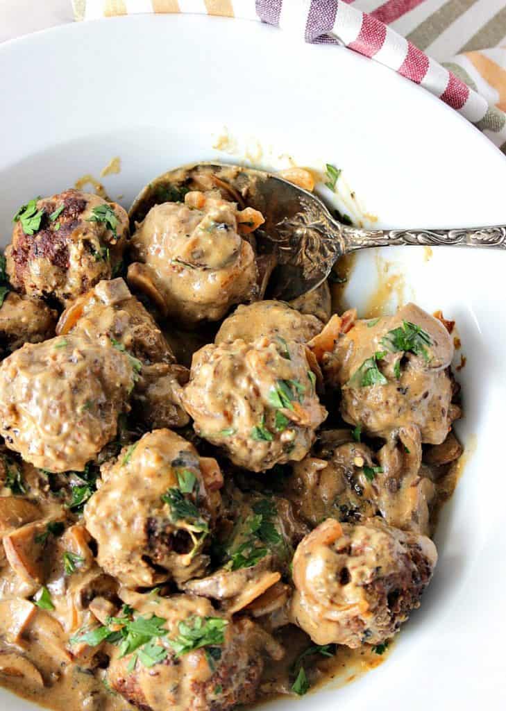 Vertical overhead photo of a bowl of German meatballs with caraway mushroom cream sauce with parsley and a spoon.