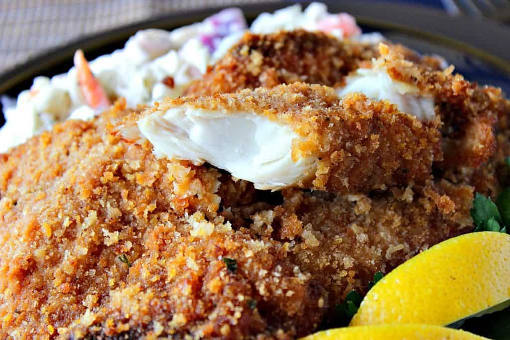 Closeup photo of the flaky inside of a fried tilapia fillet with lemon wedges.