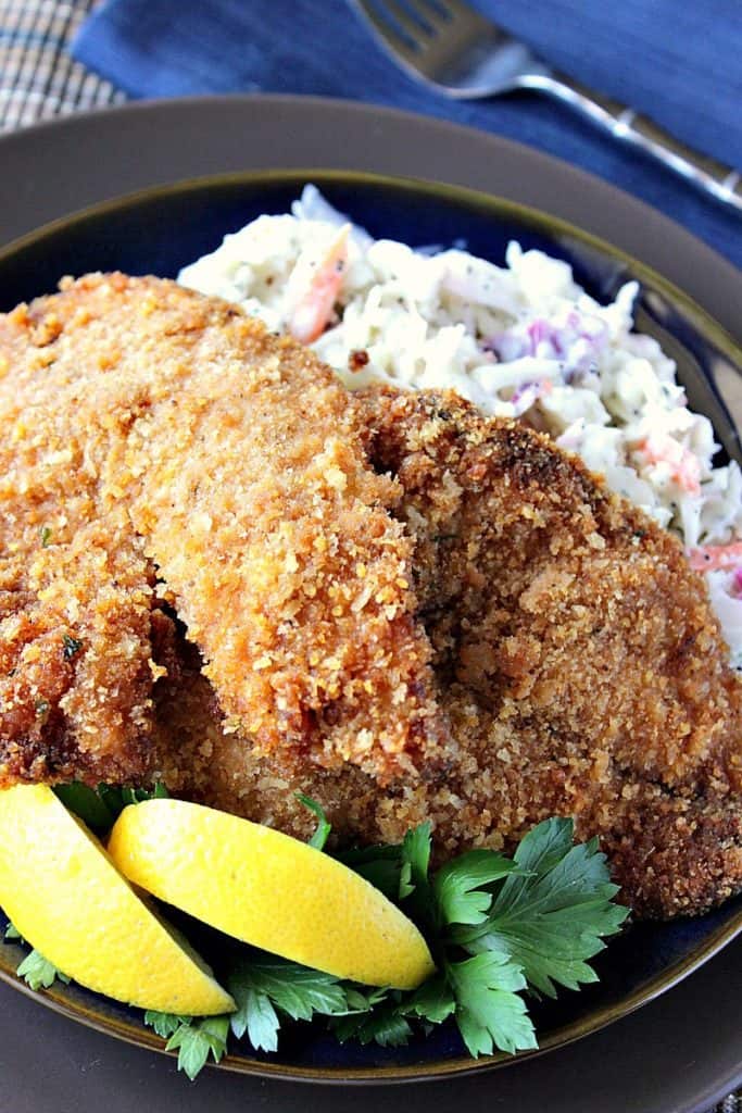 Vertical photo of crispy fried tilapia on a plate with coleslaw and a fork in the background.