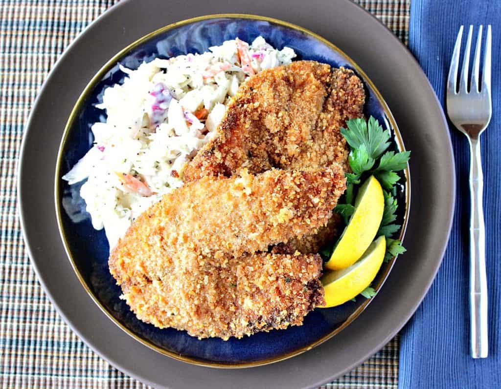 Overhead photo of a plate of homemade fried tilapia along with lemon wedges and coleslaw.