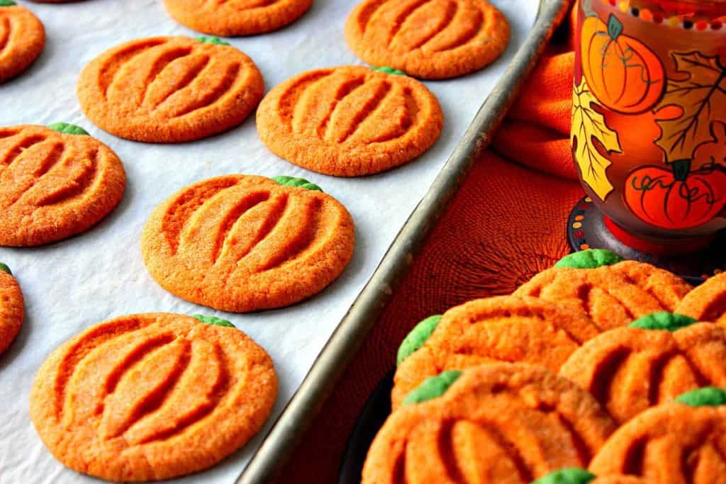 A horizontal image of a tray of pumpkin-free sugar cookies with a pumpkin and leave coffee mug.