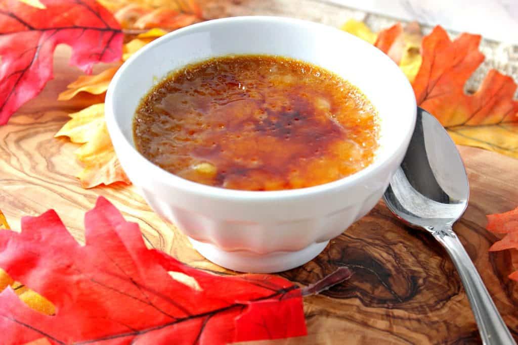 Pumpkin creme brulee in a white ramekin dish with autumn leaves and a spoon.