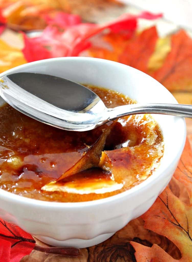 A closeup photo of a spoon on top of a cracked sugar topping from a pumpkin creme brulee.