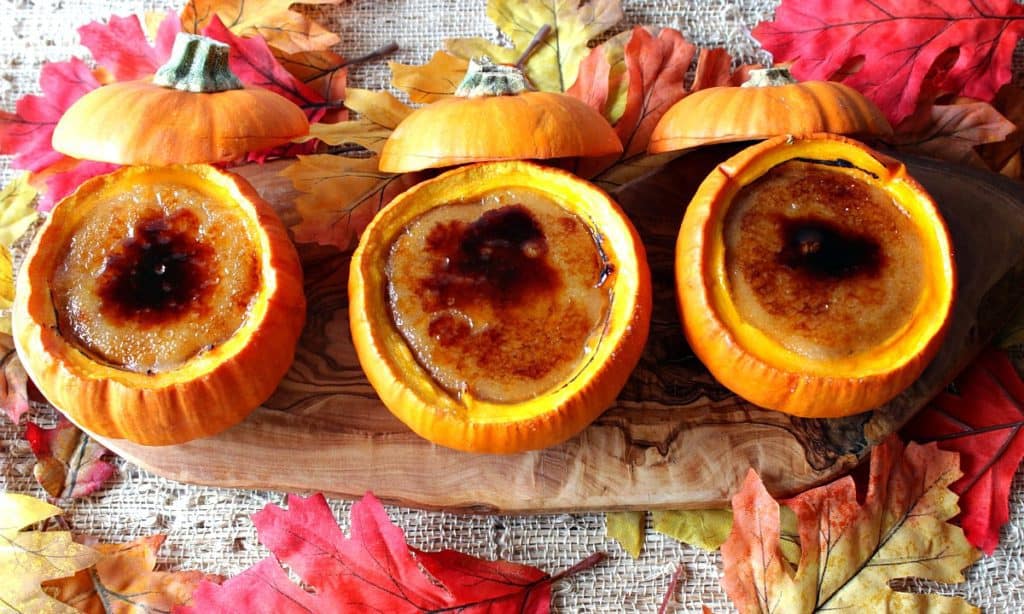 Overhead photo of three pumpkin creme brulee on a wooden board with fall leaves.