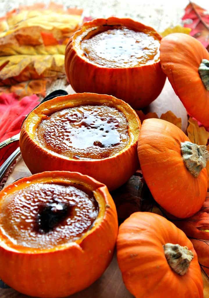 Closeup photo of pumpkin creme brulee baked in real pumpkin shells with autumn leaves and pumpkin tops.
