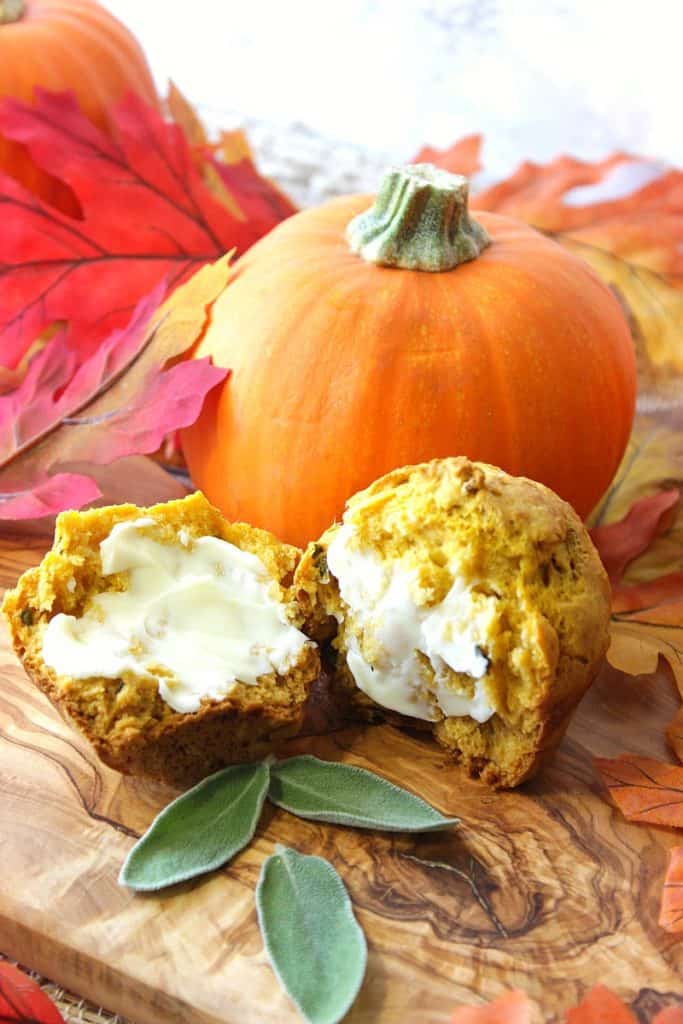 Closeup photo of a pumpkin biscuit with sage cut in half with butter and fresh sage leaves.