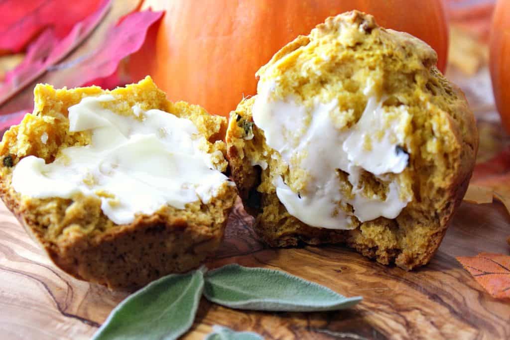 A closeup photo of a pumpkin dinner roll spread with butter and fresh sage leaves.