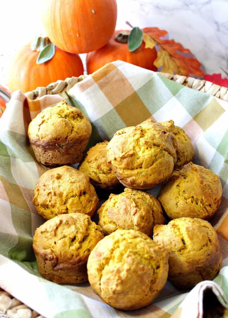 A closeup photo of a basket filled with pumpkin dinner rolls and a fall napkin.