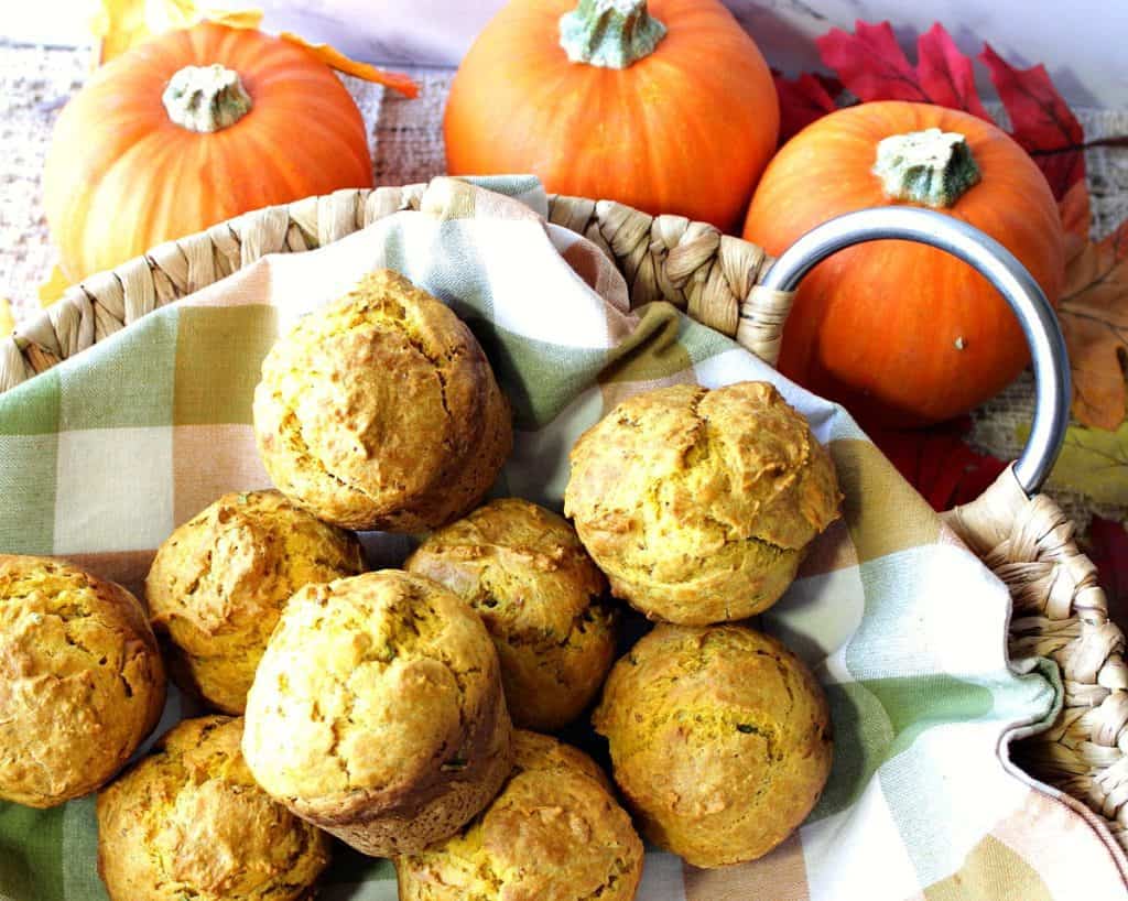 A basket filled with pumpkin sage biscuits and three small pumpkins in the background.