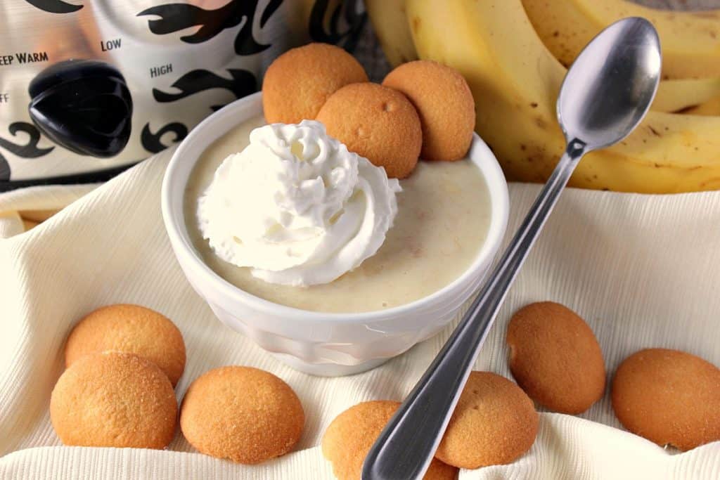 A bowl of banana coconut pudding with vanilla wafer cookies, a spoon, and a dollop of whipped cream.