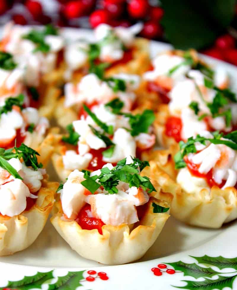 Closeup vertical photo of shrimp cocktail appetizer bites with red cocktail sauce and green parsley on a festive Christmas plate.