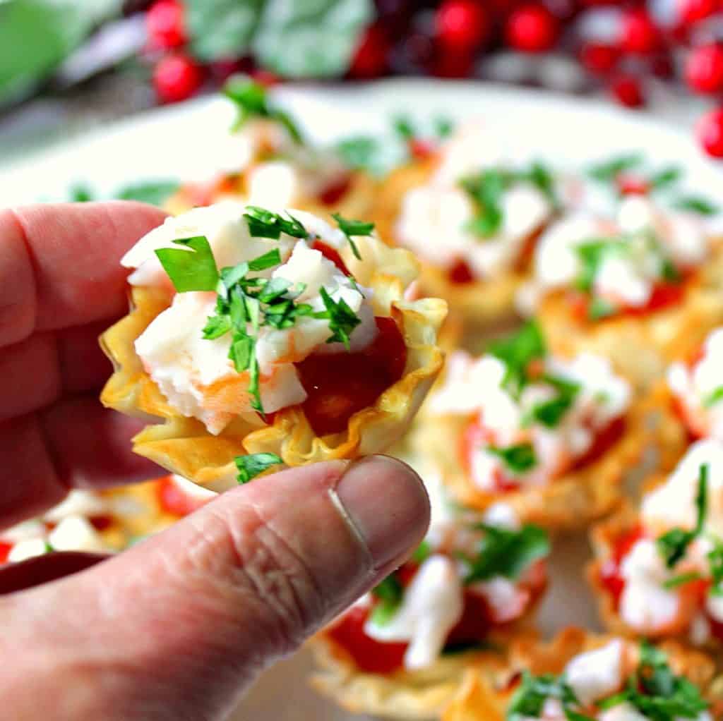 A closeup vertical photo of a hand holding a shrimp cocktail bite with parsley and chopped shrimp.