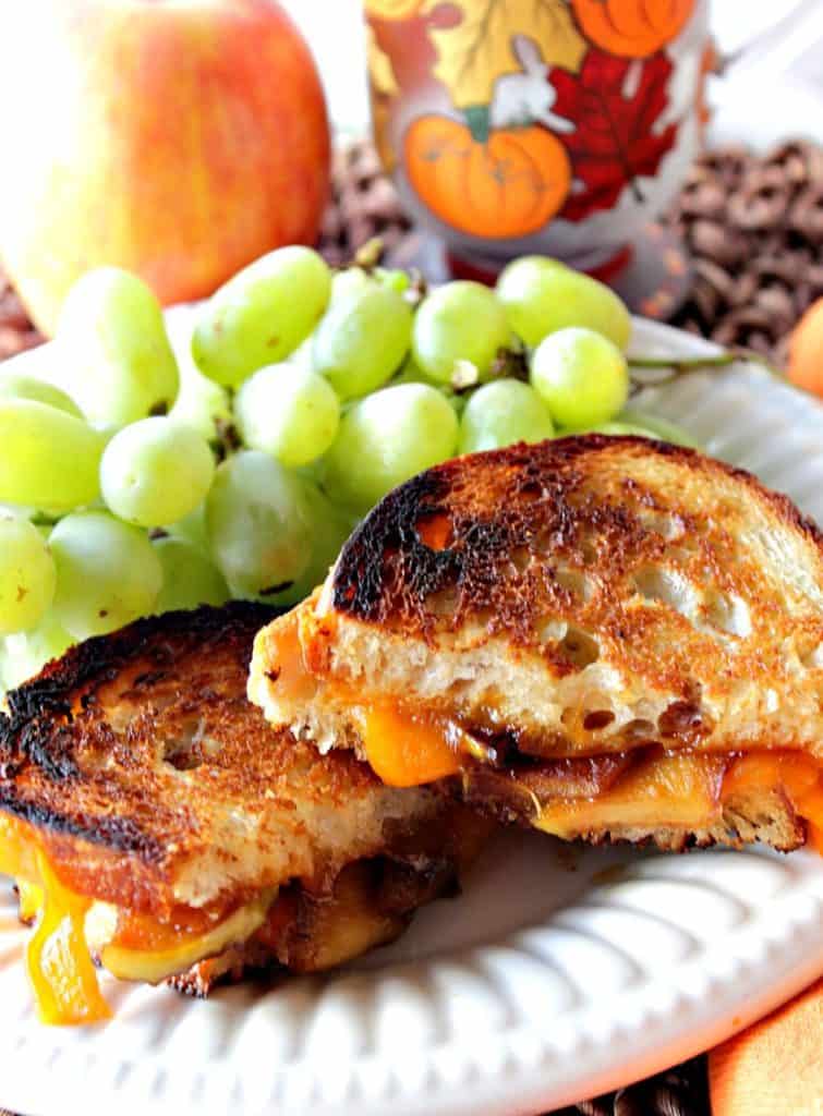 A vertical closeup photo of a grilled cheese sandwich with caramelized apples on a white plate with green grapes in the background.