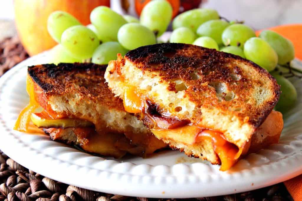 Horizontal photo of a grilled cheese sandwich sliced in half with melted cheddar cheese and caramelized apple slices.