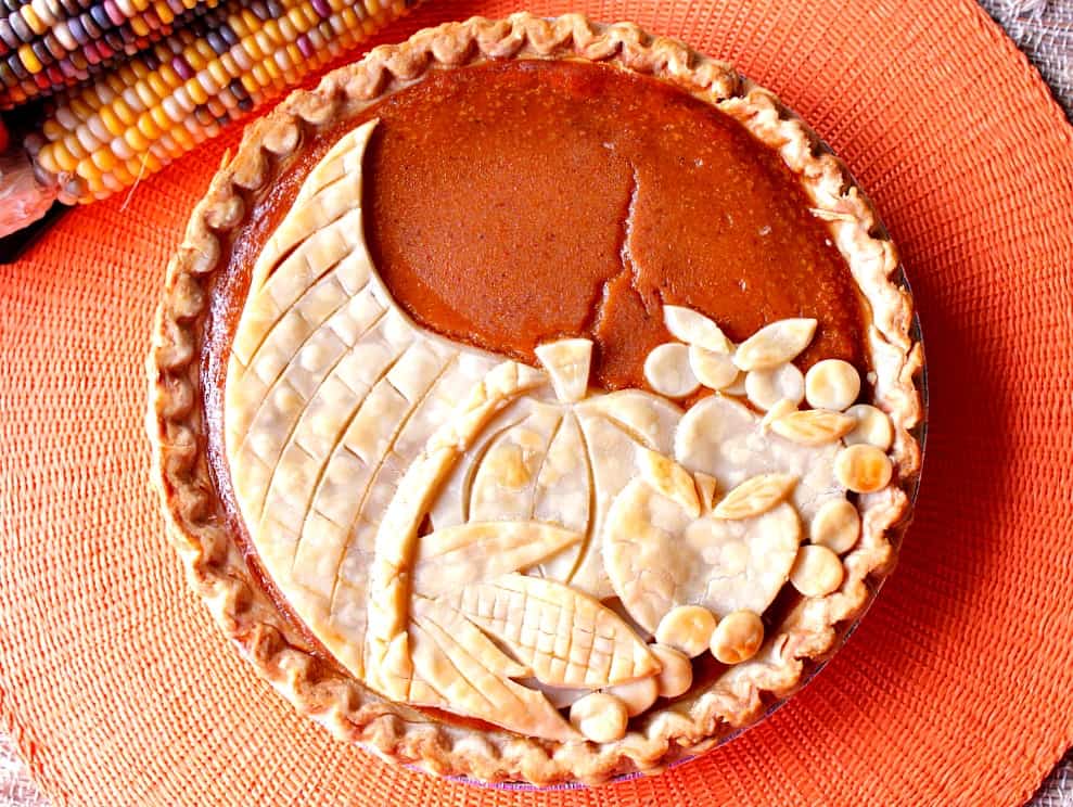 Overhead photo of a plain cornucopia pie with Indian corn on a orange place mat.