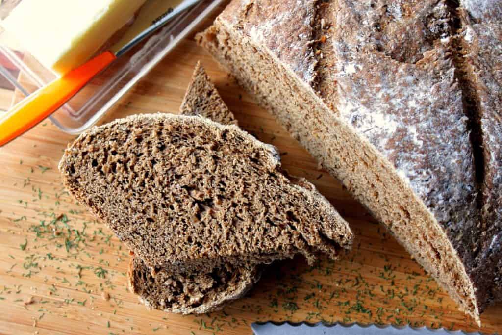 A loaf of Onion Rye Bread with Dill in a cutting board with dill weed and butter.