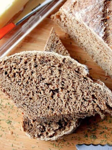 A couple of slices of Onions Rye Bread with Dill on a cutting board with dill sprinkled around.