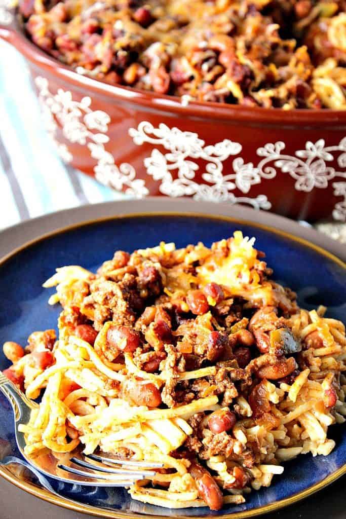 A vertical closeup image of spaghetti chili with beans on a blue plate with a casserole dish in the background.