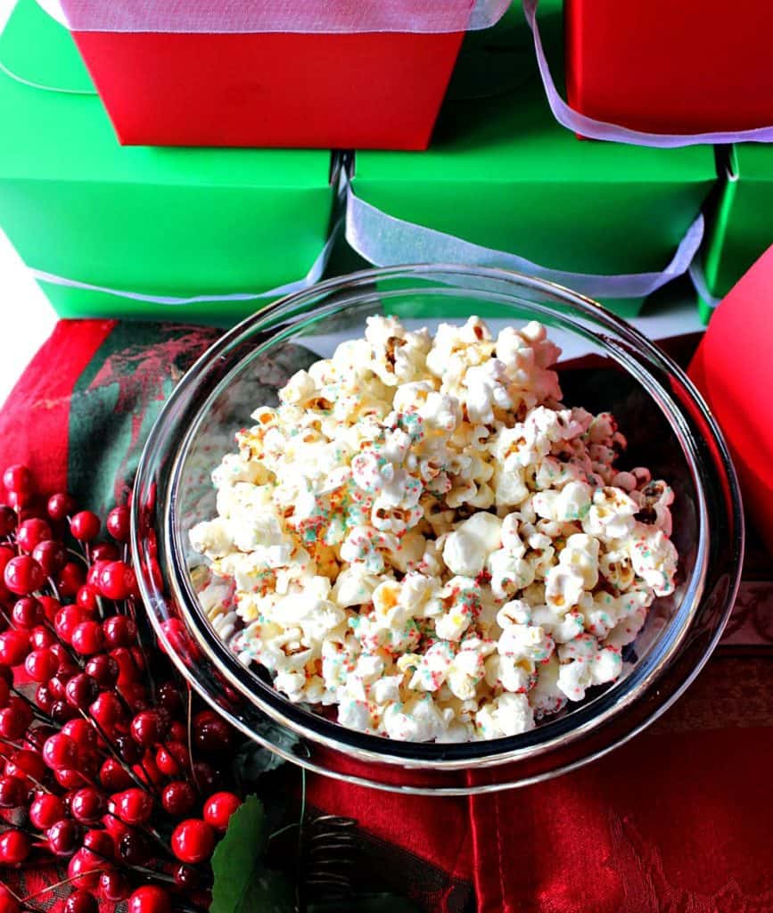 A bowl filled with White Chocolate Christmas Popcorn along with red and green boxes in the background.