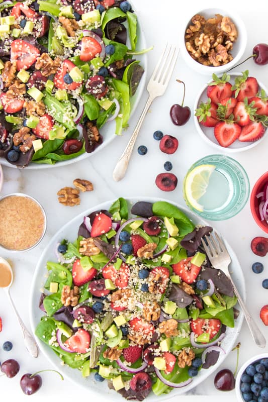 Overhead photo of a lettuce and fruit salad with strawberries and quinoa with nuts and cherries for healthy salad recipe roundup.