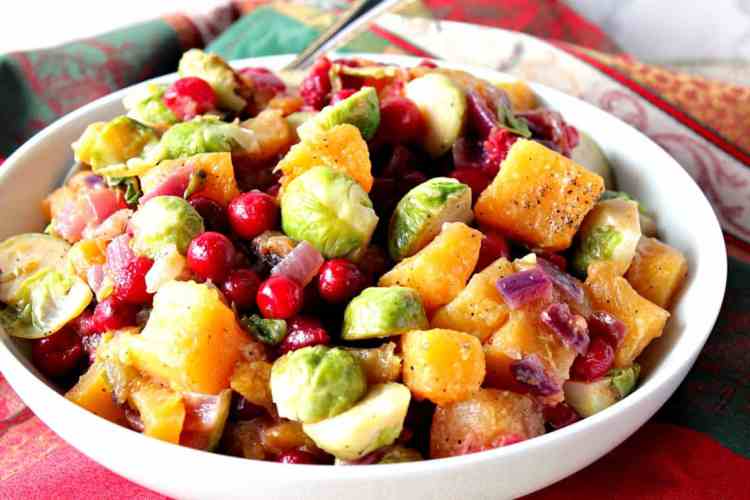 Horizontal photo of a colorful bowl of holiday sauteed vegetables with cranberries, Brussels sprouts, and butternut squash. Christmas dinner recipe roundup.