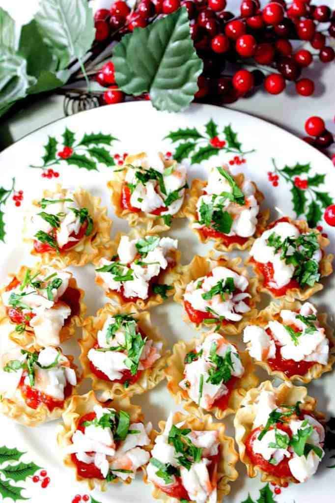Overhead vertical photo of shrimp cocktail appetizer bites on a festive holiday plate. New Year's eve appetizers and drinks recipe roundup.