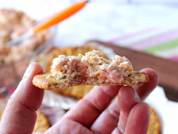 Closeup of salmon salad spread on a cracker with a bite taken out. New Years Eve appetizers and drinks recipe roundup.