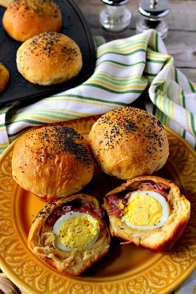 A closeup vertical image of two hard-boiled egg stuffed biscuits on a plate with a muffin in in the background with a salt and pepper shaker.