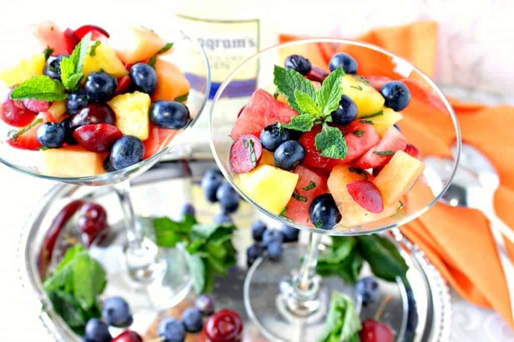 Overhead photo of two martini glasses filled with colorful fruit salad and mint.