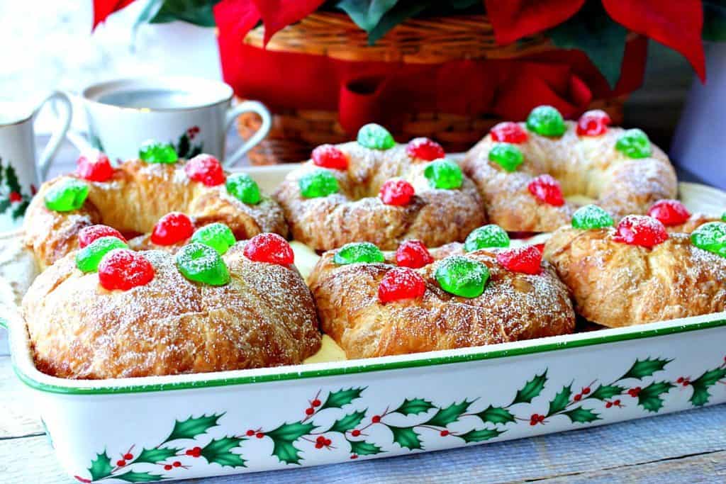 A horizontal photo of croissants in a baking dish filled with eggnog pastry cream and topped with red and green cherries for Christmas.