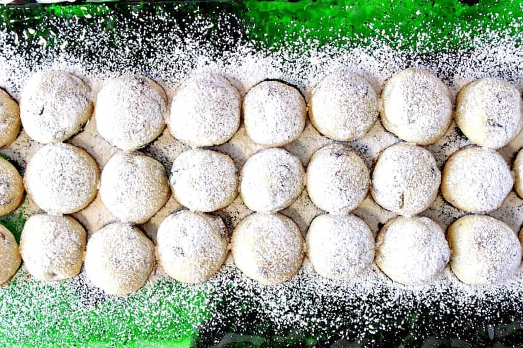 An overhead photo of a green glass plate filled with holiday snowball cookies dusted with confectioners sugar.